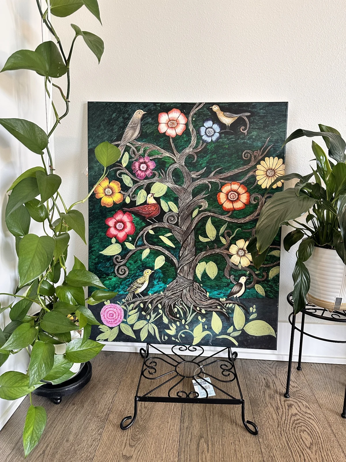 An original painting of birds, flowers and a branching tree, photographed among houseplants